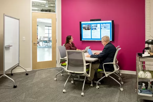 Two people in meeting space looking over laptops